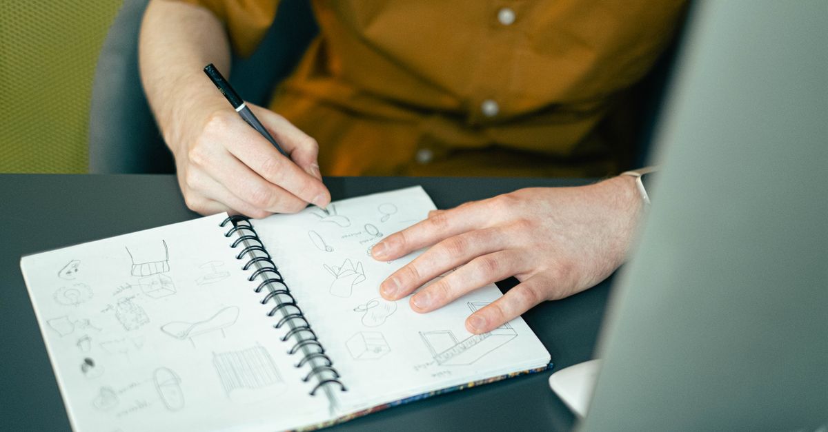 Close-up of a designer sketching ideas in a spiral notebook at a desk, highlighting creativity.